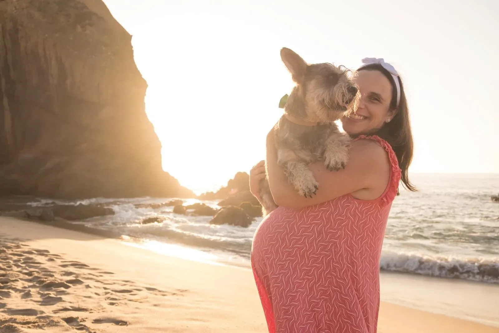 Grávida com o cão ao colo na praia ao pôr do sol